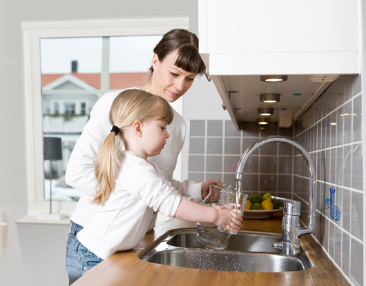 Eine Mutter füllt mit ihrer Tochter ein Glas Wasser an der Spüle auf. 